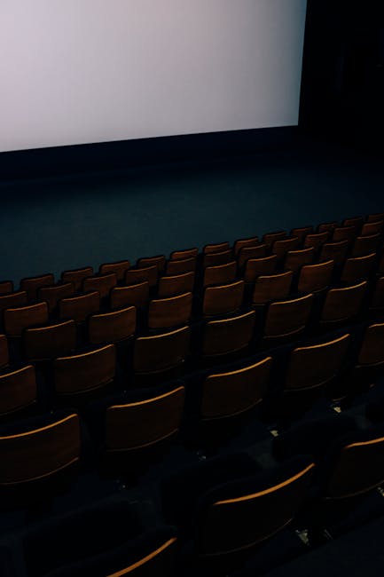 pexels-photo-3709369-3709369 A dark and empty theater auditorium with rows of seats and a large screen.